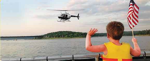 Image of a child holding the american flag waving to a helicopter over a lake.